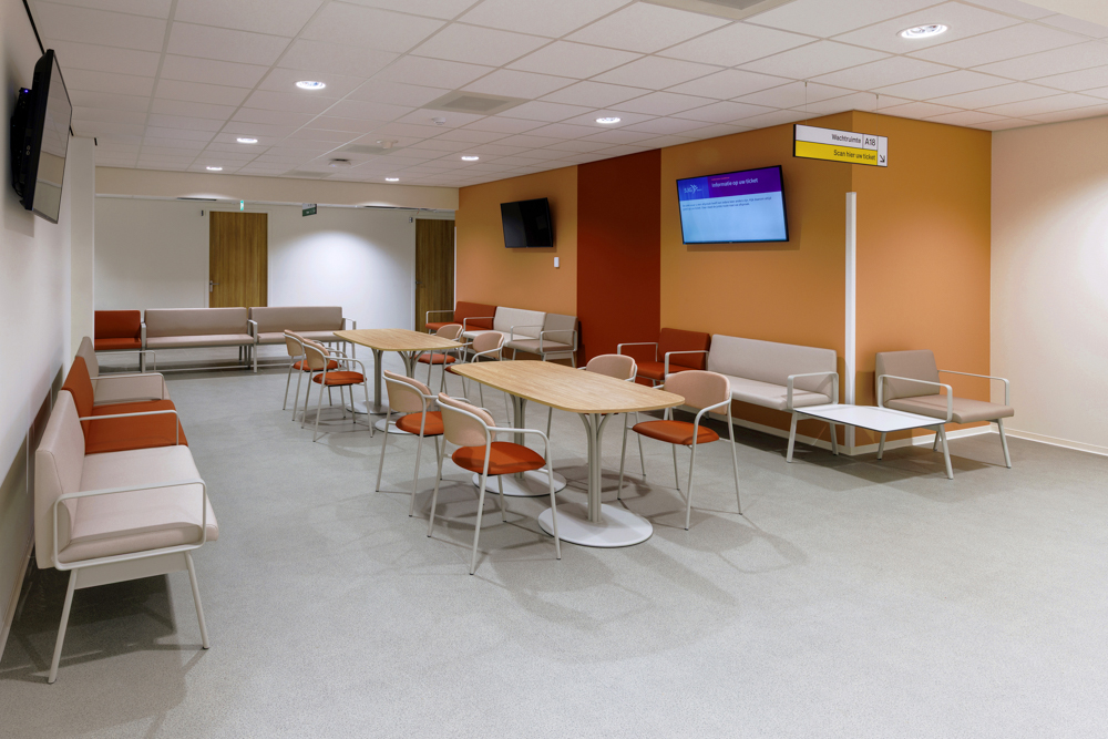 Moderne wachtruimte in ziekenhuis SJG Weert met zitbanken, stoelen, tafels en informatiescherm.
