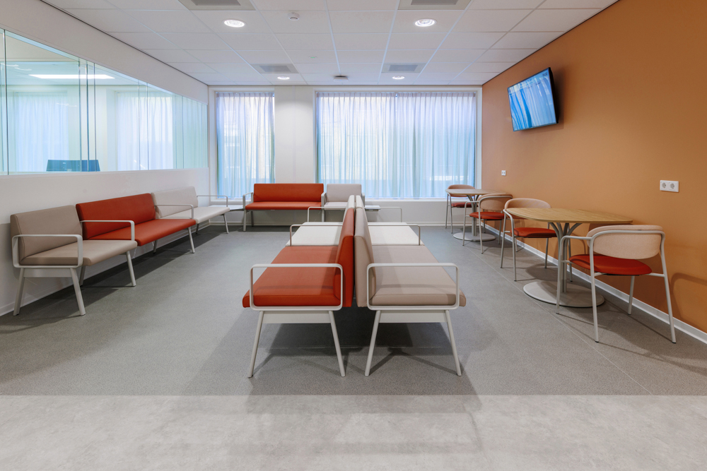 Moderne wachtruimte in ziekenhuis SJG Weert met zitbanken, stoelen, tafels, gordijnen en informatiescherm.